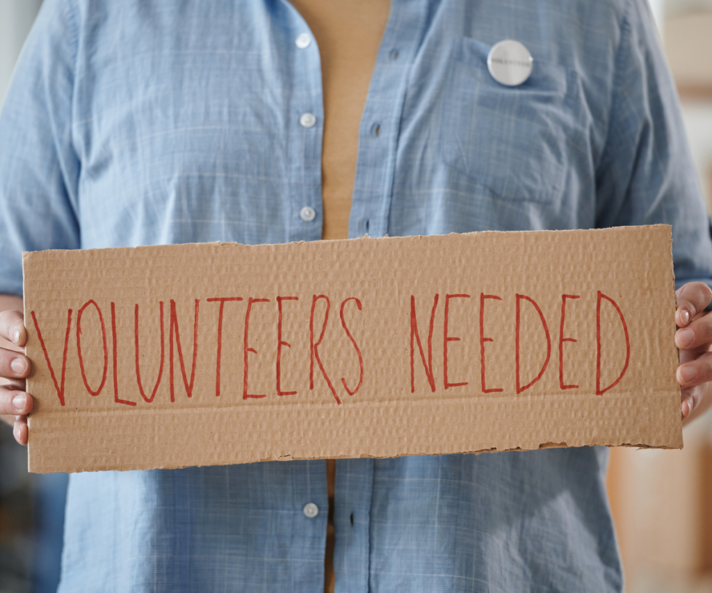 Person holding sign that says: volunteers needed.